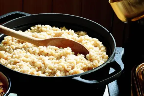 Un mestolo di legno affonda in una pentola piena di fumante orzo perlato, pronto per essere servito.