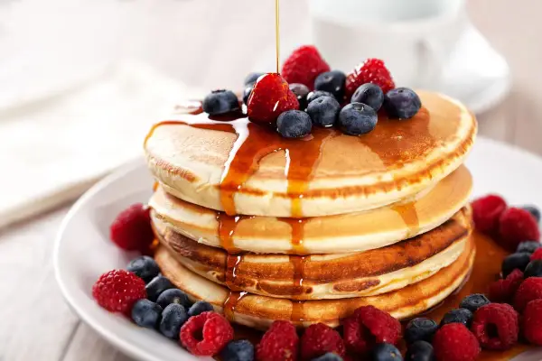 Pancake ricetta: una pila di soffici pancake guarniti con sciroppo d'acero, lamponi e mirtilli freschi.